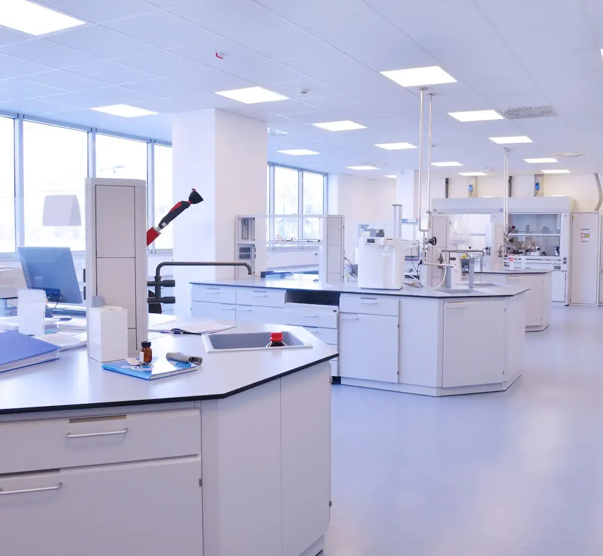 Vue d’un laboratoire propre avec établis blancs, matériel de bureau et instruments de chimie sur les plans de travail.